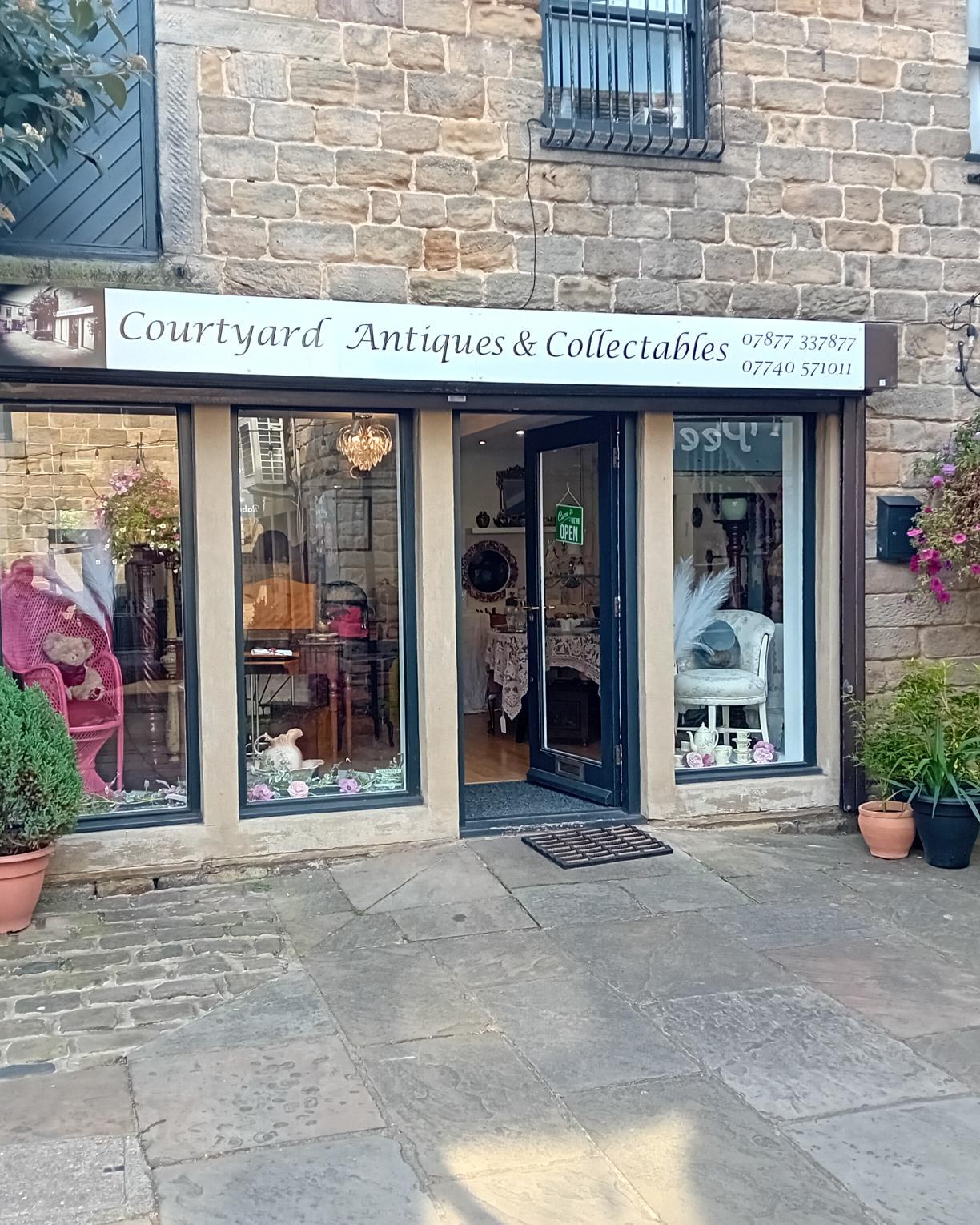 The bright stone storefront of Courtyard Antiques & Collectables on the cobbled courtyard in Otley, with open door and window displays